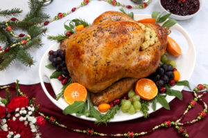 Roasted herb rubbed turkey garnished with fresh grapes, oranges, and cranberry is ready for Christmas dinner. Ornaments, Champagne, candles, and other Christmas decorations on feast table.
